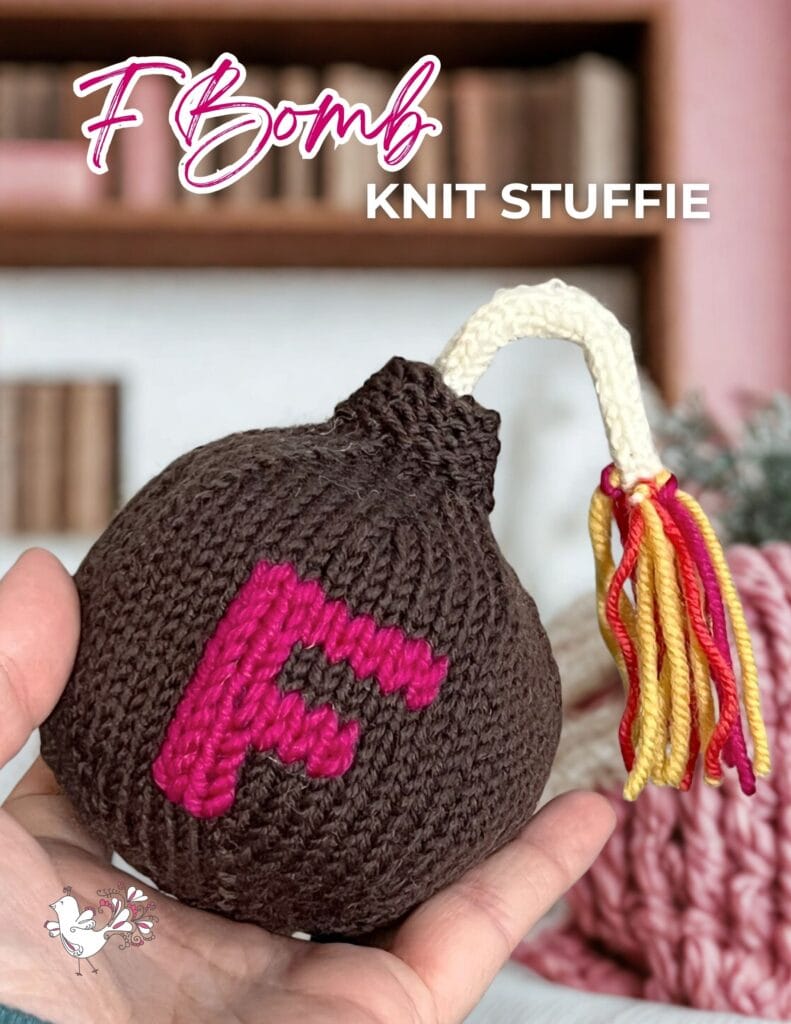 A hand holds a knitted bomb-shaped stuffie with a pink letter "F" and a multicolored fuse. The text reads "F Bomb KNIT STUFFIE." Books and yarn, perfect for finding free knitting and crochet patterns, are blurred in the background. -Marly Bird