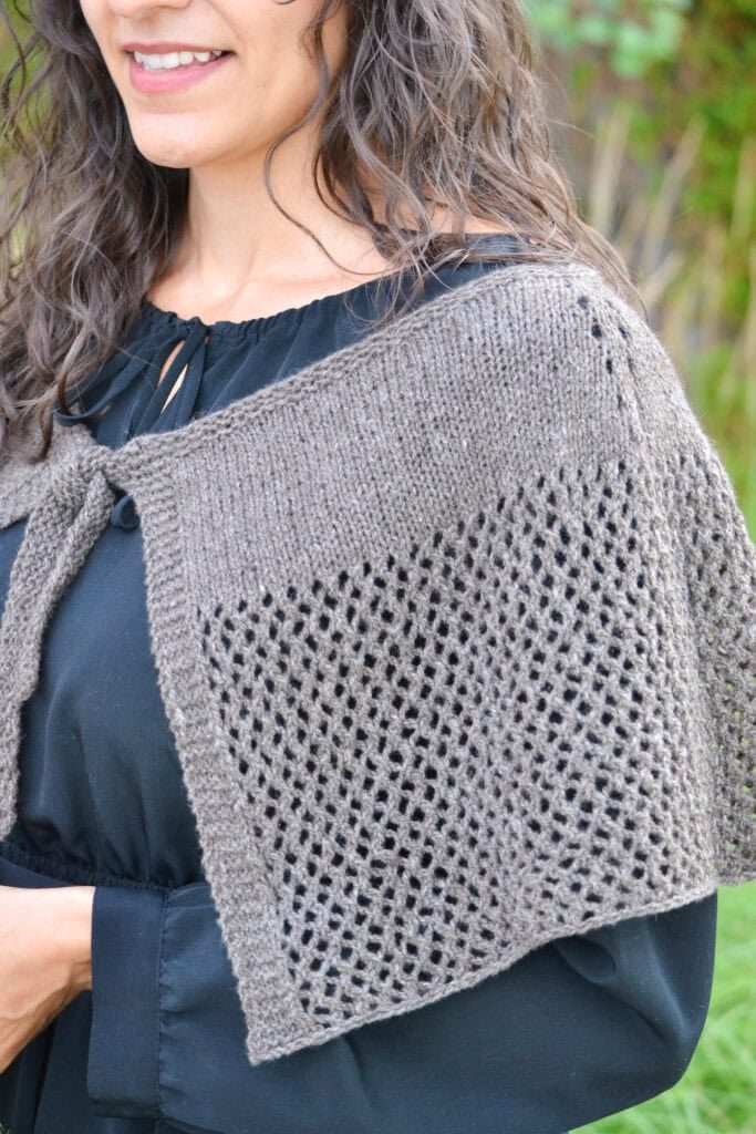 Gray lace-patterned knitted Blood of My Blood Shawl shown worn over black blouse, highlighting stitch detail and drape.