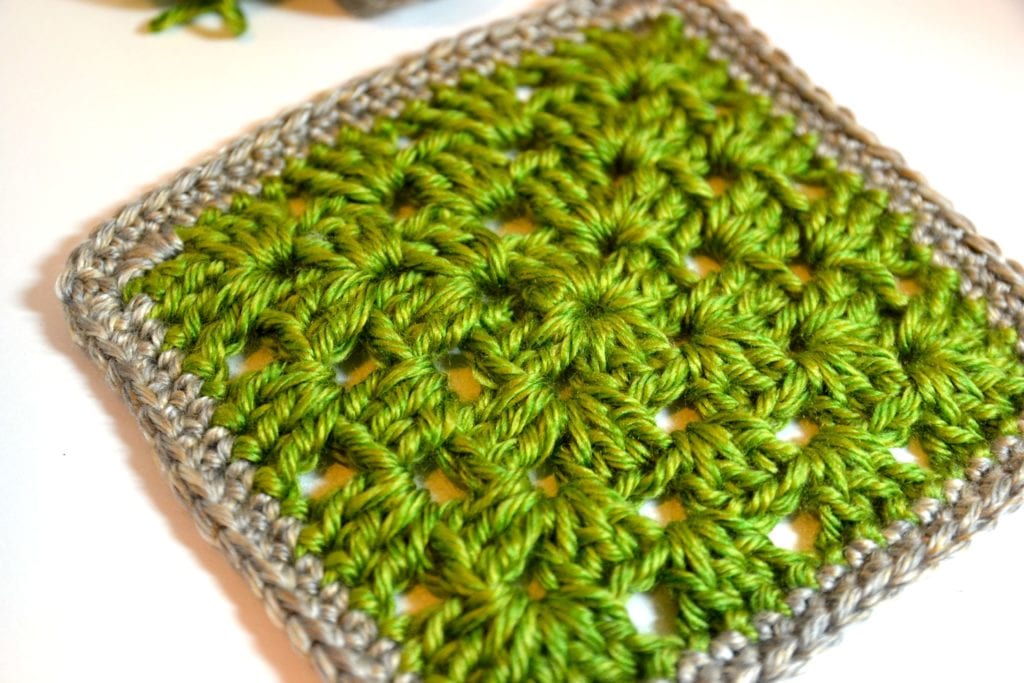 A close-up of a crochet granny square with vibrant green and subtle gray yarns, showcasing intricate patterns and textures on a light background. -Marly Bird