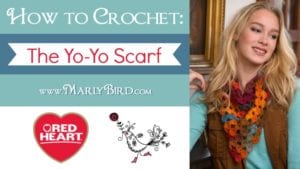 Promotional image for a crochet tutorial featuring a smiling woman wearing a colorful scarf, with text "How to Crochet: The Yo-Yo Scarf" and logos for Marly Bird and Red Heart. -Marly Bird