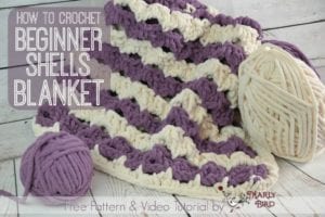 Image shows a crochet beginner shells blanket in white and purple yarn, with text promoting a free pattern and video tutorial by Marly Bird. Additional yarn balls are visible. -Marly Bird