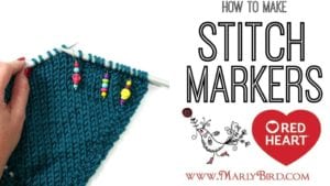 A person's hand holding a blue knitted fabric with colorful stitch markers on needles; an inset displays text "How to Make Stitch Markers" with Red Heart logo and MarlyBird.com. -Marly Bird