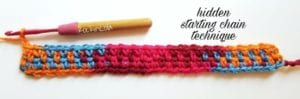 A colorful crocheted piece with a hidden starting chain technique, featuring alternating stripes of blue and pink. A wooden crochet hook rests on the left. Text overlay: "Hidden Starting Chain Technique. -Marly Bird