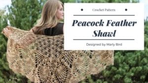 A woman showcases a large, delicately crocheted shawl resembling a peacock feather, designed by Marly Bird, against a backdrop of green foliage. Text overlay describes it as a Crafty is Cool crochet pattern. -Marly Bird