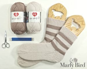 Beige and cream yarn, needles, scissors, and a pair of striped hand-knit socks displayed on wooden sock blockers.