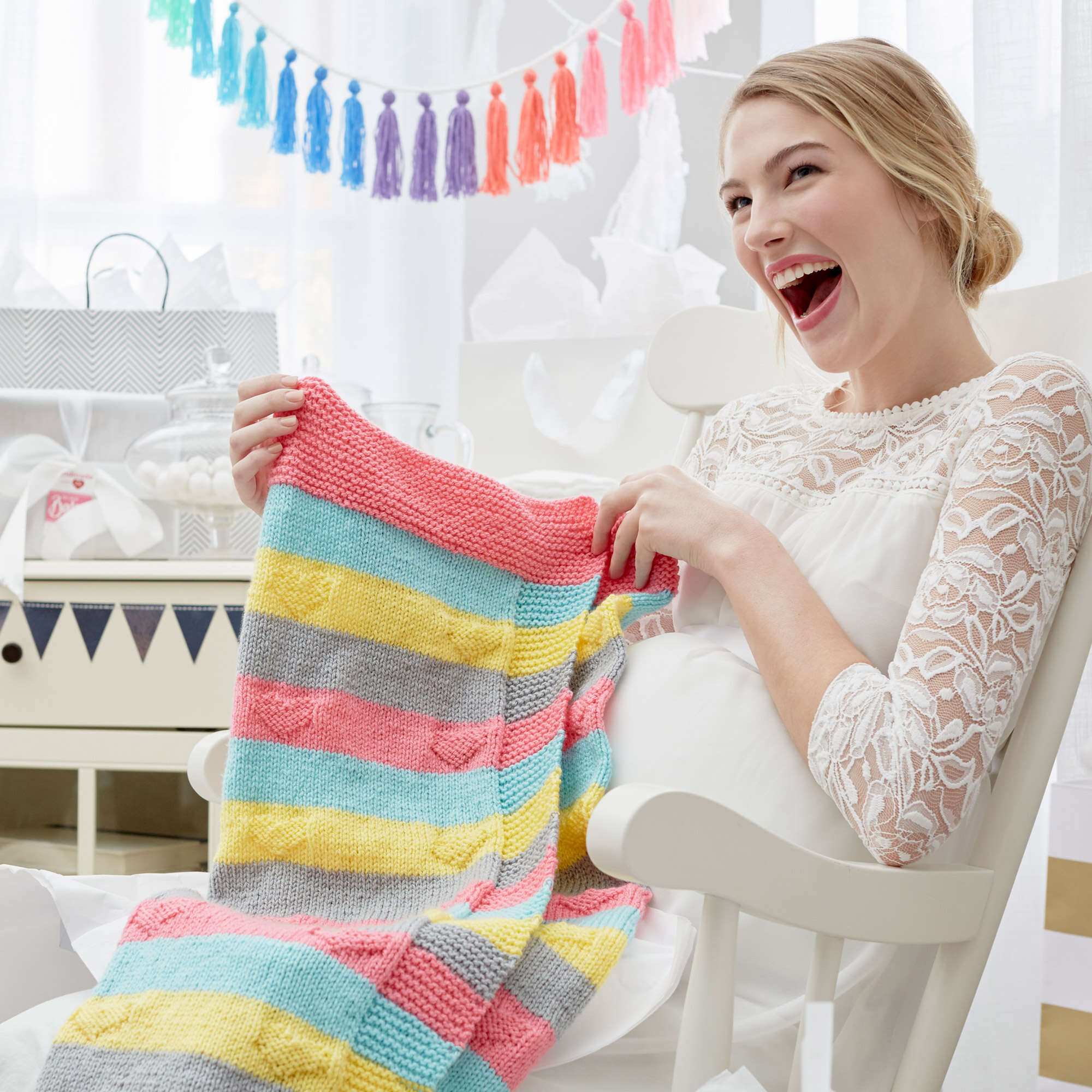 woman in rocking chair holding up the knit sample of the love you knit baby blanket pattern. marly bird