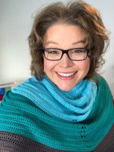 Marly Bird wearing the bluebonnet crochet shawl around her shoulders. Shawl is light blue, tea. and a dark charcoal gray.