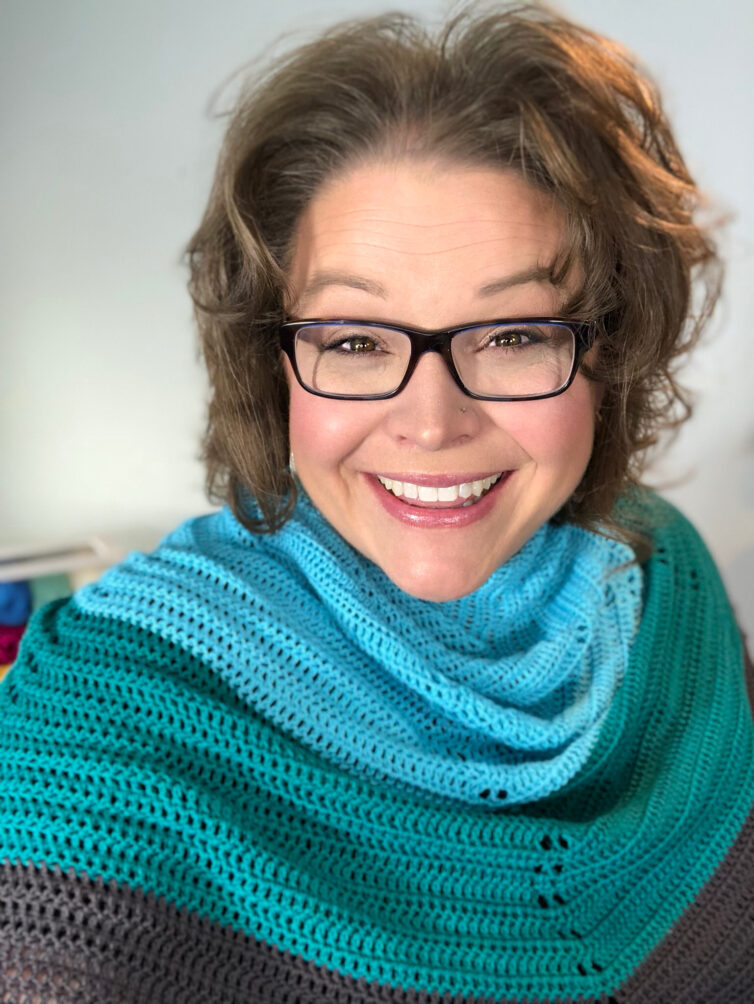 Marly Bird wearing the bluebonnet crochet shawl around her shoulders. Shawl is light blue, tea. and a dark charcoal gray.