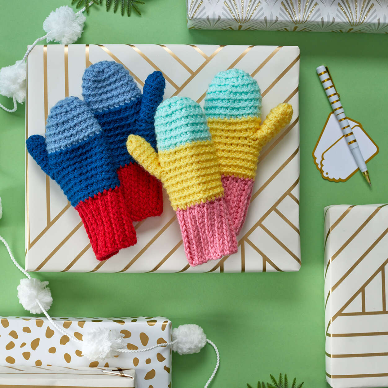 Snowday Crochet Mitten Pattern shown in to sets of different colors displayed on wrapped presents - Marly Bird