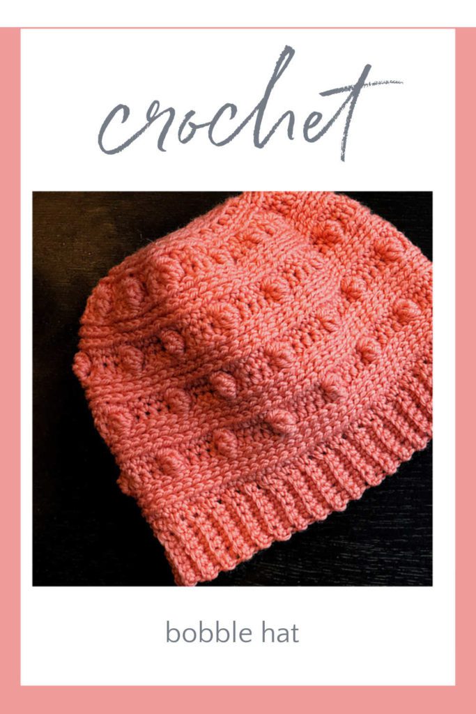 Bobble crochet hat free pattern: coral colored crochet hat with alternating stripes of bobbles and knit-look stitches, on dark background.