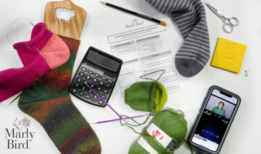 Picture of finished toe up knit socks and partially finished toe up knit socks, a calculator, a worksheet, and iphone with camera image of marly bird