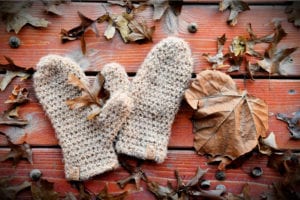 A pair of knitted mittens lying amid scattered autumn leaves and acorns on a wooden surface, featuring a pattern from Marly Bird. -Marly Bird