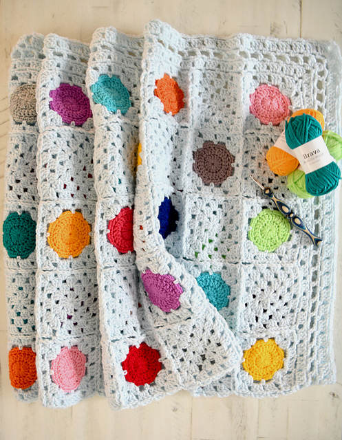 confetti dots granny blanket pattern by marly bird. Show artfully displayed on a flat surface with 3 balls of yarn and a crochet hook.