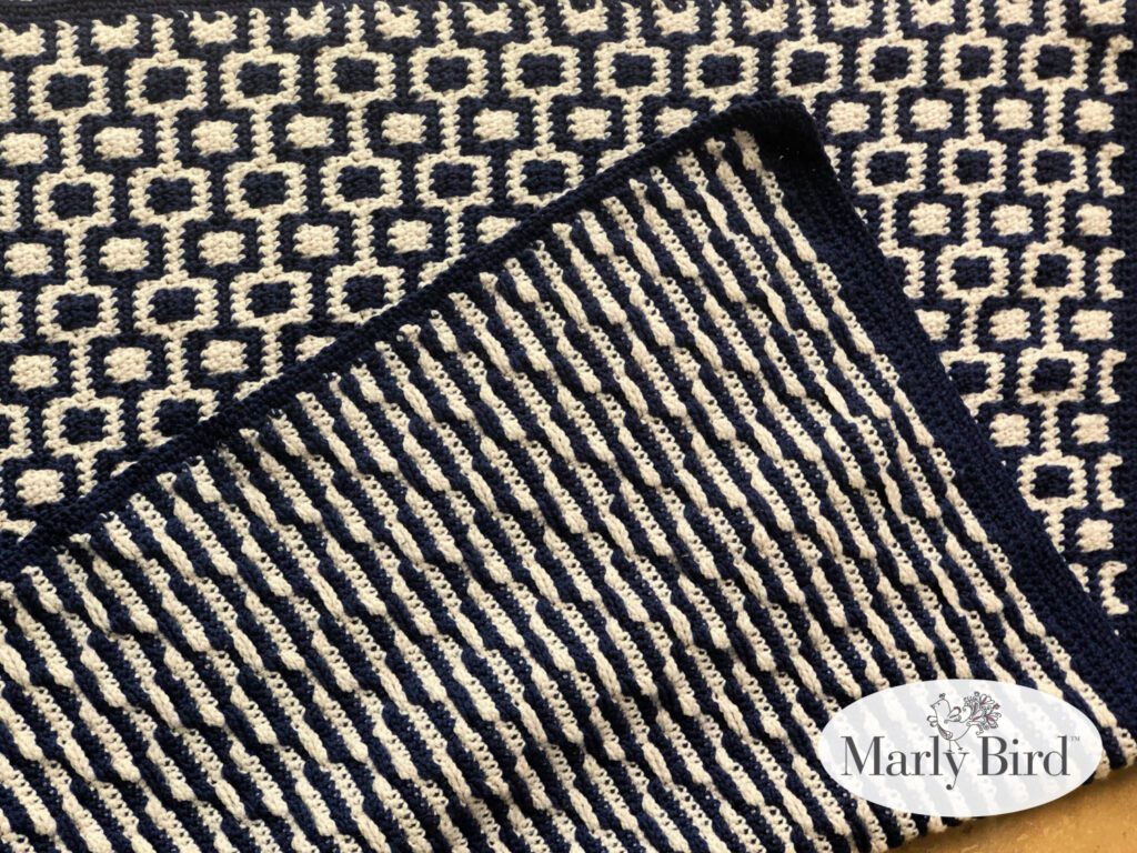 Close-up of a blanket featuring mosaic crochet with a two-tone pattern in navy and cream; geometric designs on top and striped texture on the bottom, showcasing detailed stitch work. -Marly Bird