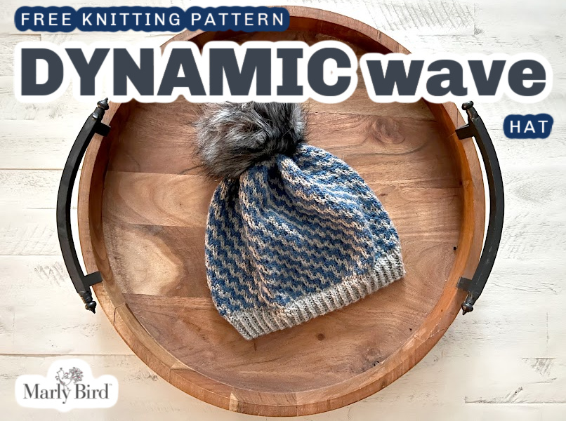 A stylish mosaic knit beanie with a fluffy pom-pom resting on a round wooden tray, ready to be presented as a handmade gift. Dynamic Wave Mosaic Knit Hat pattern by Marly Bird
