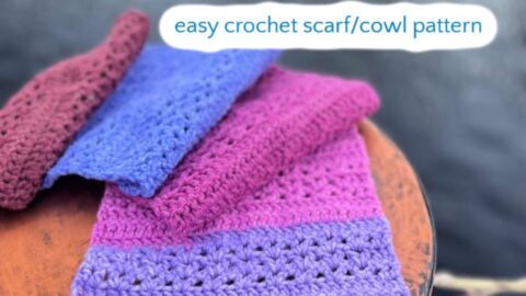 Crochet scarf in purple, pink, and blue draped on a round surface by water; shows textured stitch detail.