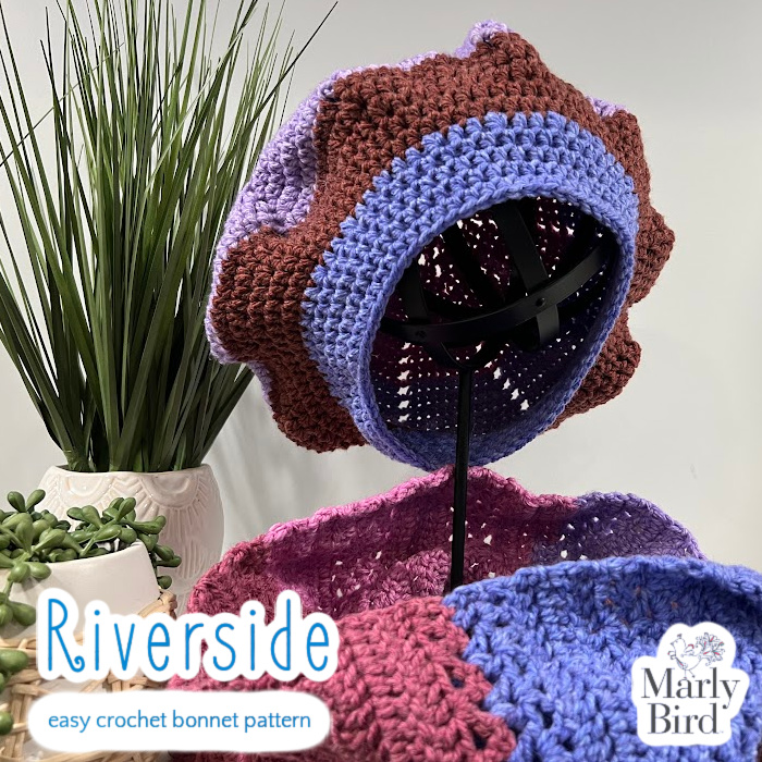 View of brim and inside of Riverside Bonnet on black metal stand, with Riverside Cowl around stand base, with potted plants. Marly Bird 