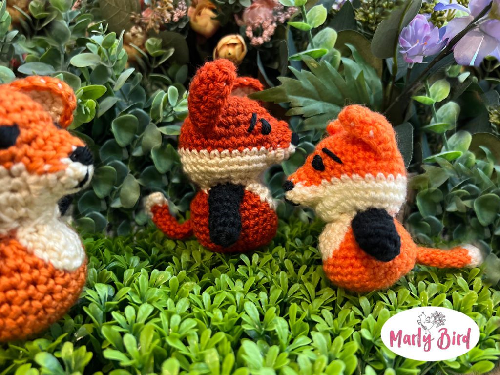 Apricot Lane Amigurumi character Felix the Fox in three different sizes. All use the same Felix the Fox crochet stuffie pattern but different size yarn and hook. The image shows each side view of the fox against green leaf and floral background.