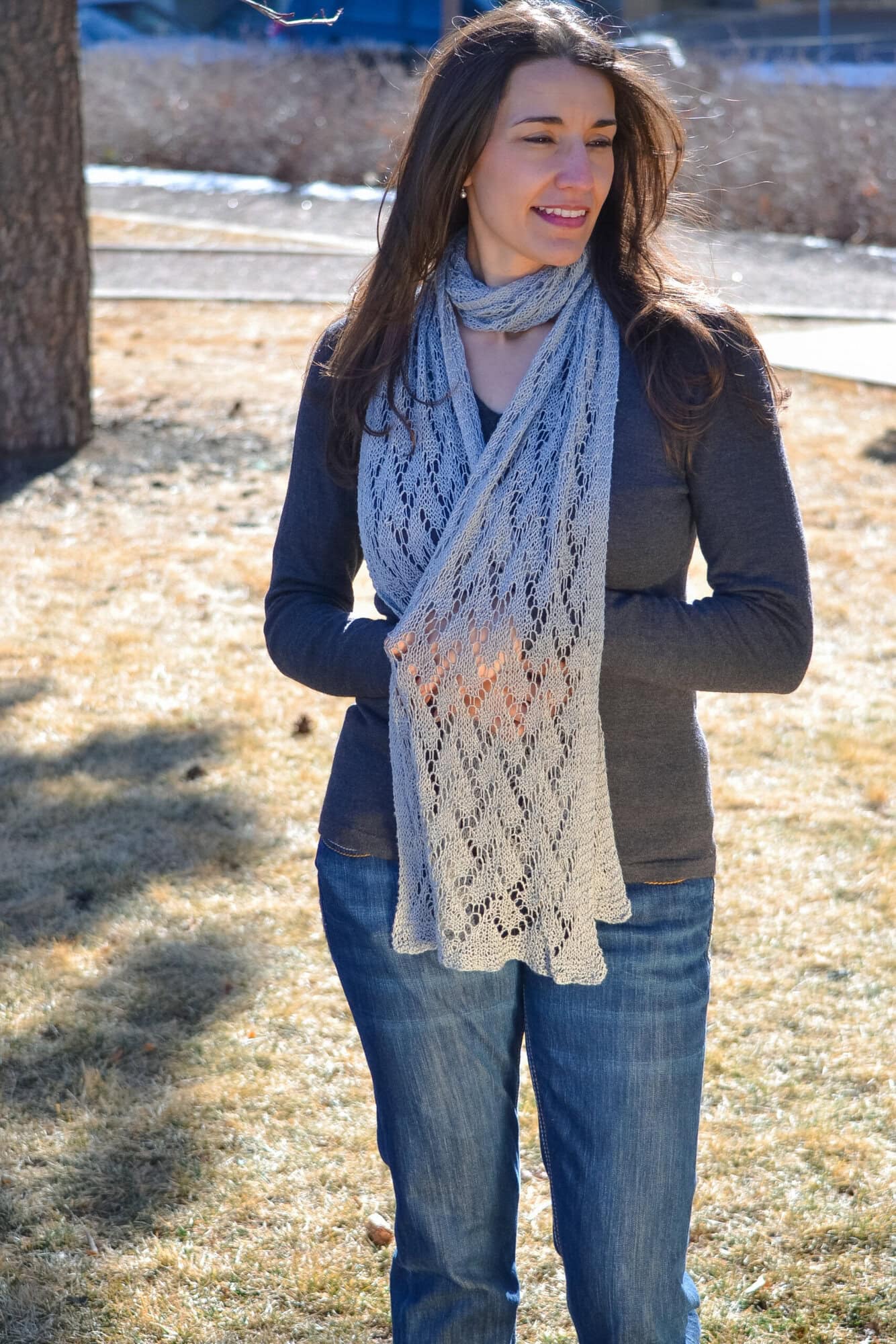 Marly Bird wearing the Shangri-La free knit lace scarf pattern crossed at the chest in soft gray.