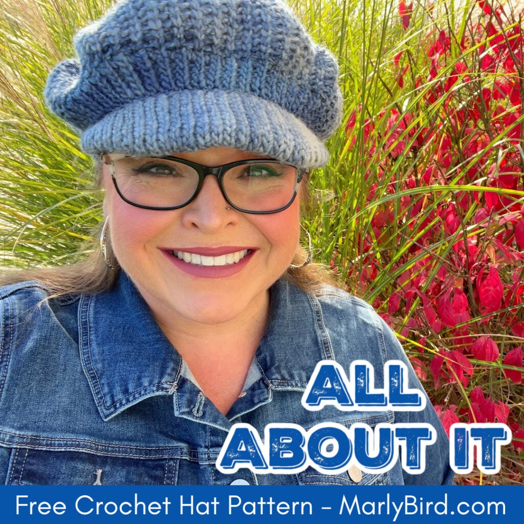 Marly Bird wearing the blue All About It crochet newsboy hat outdoors with colorful fall foliage, overlaid with text reading All About It Free Crochet Hat Pattern MarlyBird.com. -Marly Bird