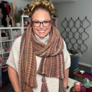 A person models a chunky, multicolored almond brittle knit wrap, highlighting the cozy texture and color transitions.