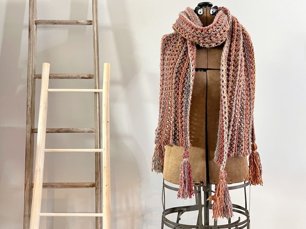Bulky knit lace scarf with tassels displayed on mannequin, highlighting its openwork texture and drape.