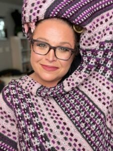 Woman wearing a purple, black, and white knit sweater with mosaic motif; textured stitches and vibrant pattern visible. Fingering weight knit mosaic triangle shawl worked corner to corner