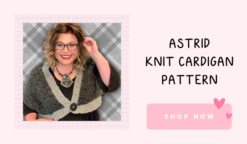 A person wearing glasses and a black outfit, layered with a gray knit cardigan, stands smiling. Against a checkered backdrop, the text reads "Astrid Knit Cardigan Pattern - JOANN FALL Stitch Along 2024" with a "Shop Now" button and pink hearts. -Marly Bird