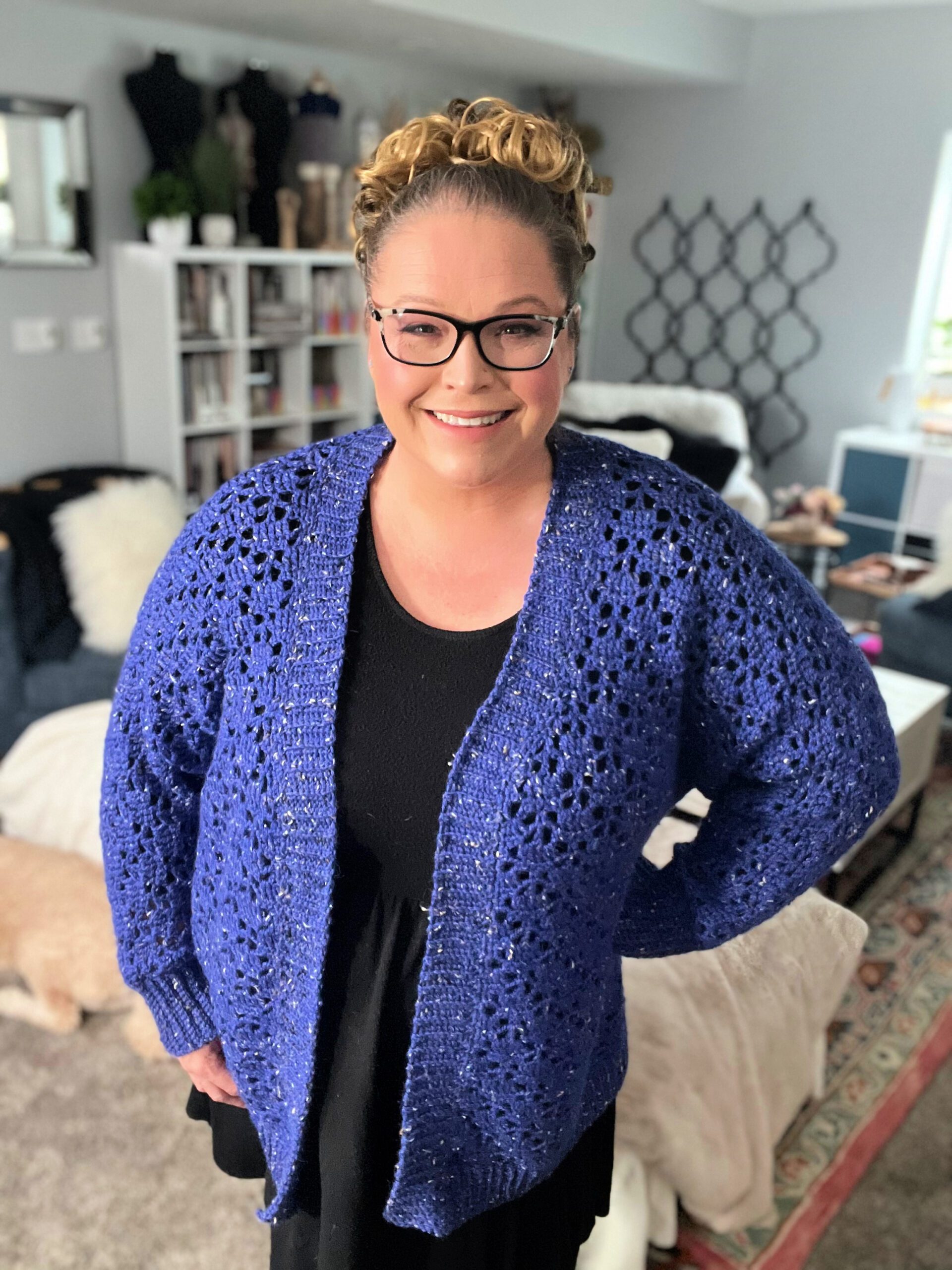 Marly Bird beams with joy, modeling her Aurora Lace Crochet Cardigan in cobalt blue, showcasing the bold lacework and cozy ribbed edges of this handmade garment.