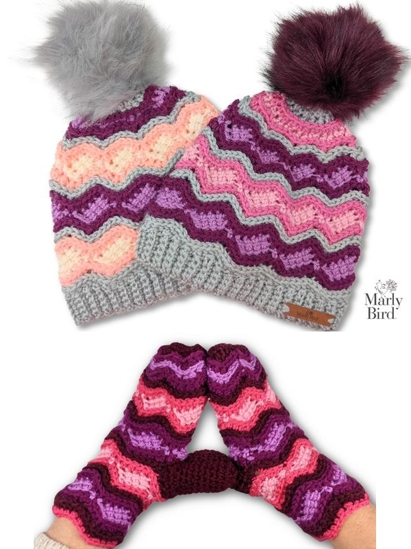 Bavaria Hat & Mittens - rippled and  striped in grey, plum, lilac, pink, light pink yarn. 2 hats in similar colorways, one with grey fur and one with plum fur pompom. Mittens below with plum yarn as main color. White background.