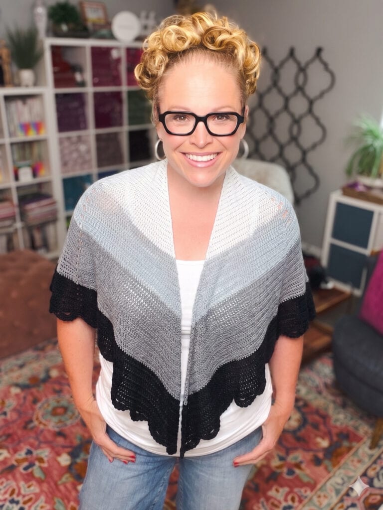 Woman modeling a bluebonnet crochet lace shawl, showing openwork stitches and drape, worn over a white top and jeans.