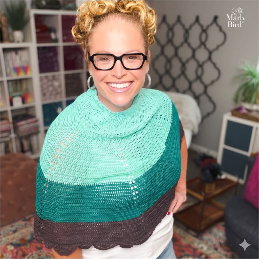 Woman modeling a crochet lace shawl in teal and brown, highlighting delicate stitching and drape. "Marly Bird" in corner.