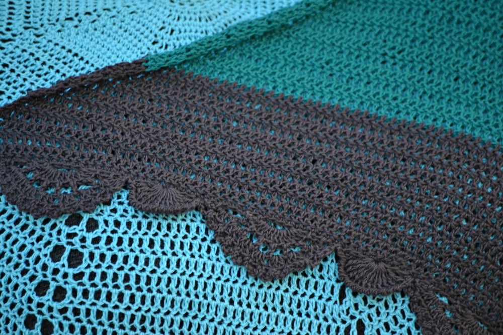 Crocheted fabric with teal and brown yarn, showing intricate patterns, clear scalloped edging, and visible texture.