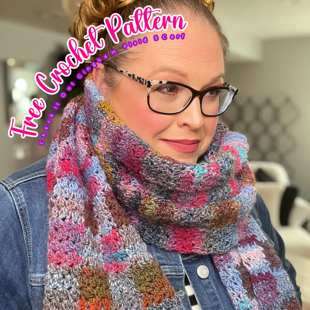 A woman with glasses smiles while showcasing a colorful, chunky crochet scarf. She wears a denim jacket and her hair is pulled back. The text overlay reads "Free Crochet Pattern for Puffed Scarf, check it out at crystalnpaula.com." The background is an indoor setting with cozy vibes. -Marly Bird