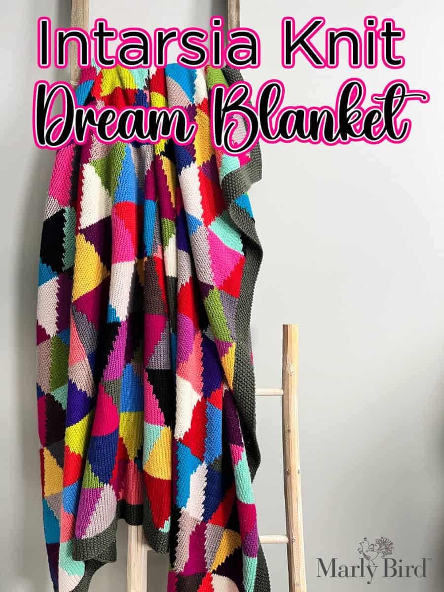 A chic intarsia knit blanket with vibrant geometric patterns is elegantly draped over a wooden ladder. The text "Chic Sheep Dream Intarsia Blanket" graces the top, while a logo featuring "Marly Bird" sits in the bottom right corner. -Marly Bird