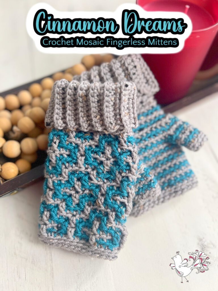 Crochet fingerless mittens in gray and teal with a mosaic pattern are artfully displayed. Titled "Cinnamon Dreams," these cozy creations rest beside a red container brimming with wooden beads. A charming bird doodle graces the corner, hinting at the delightful free pattern available. -Marly Bird