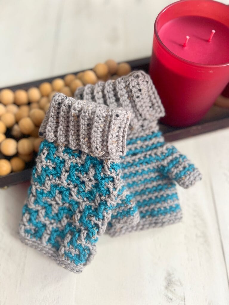 Crochet mosaic fingerless mittens with intricate stitched patterns, displayed beside a lit candle.
