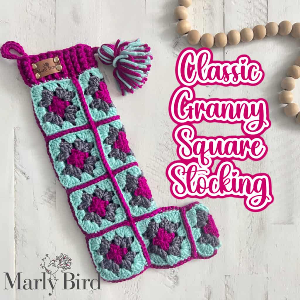 A handmade stocking made of crochet granny squares in turquoise, purple, and magenta lies on a white surface. It features a crochet loop and a tassel. "Classic Granny Square Stocking" is written in bold pink text beside it, offering inspiration for your next project with its free pattern charm. -Marly Bird