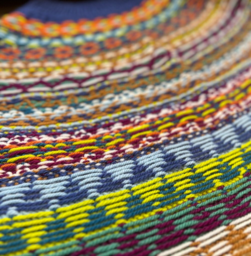 The image presents a close-up view of the inside-out aspect of a stranded knit pattern, known colloquially among knitters as "float porn." The term celebrates the often unseen side of colorwork knitting, where the carried yarns, or "floats," create their own intricate pattern on the reverse side of the fabric. This view showcases a tapestry of intertwined yarns in a kaleidoscope of colors, highlighting the complex craftsmanship and attention to detail that goes into such knitting work. The vibrant strands crisscross in harmony, revealing the structural beauty and skill that Marly Bird's patterns are known for.