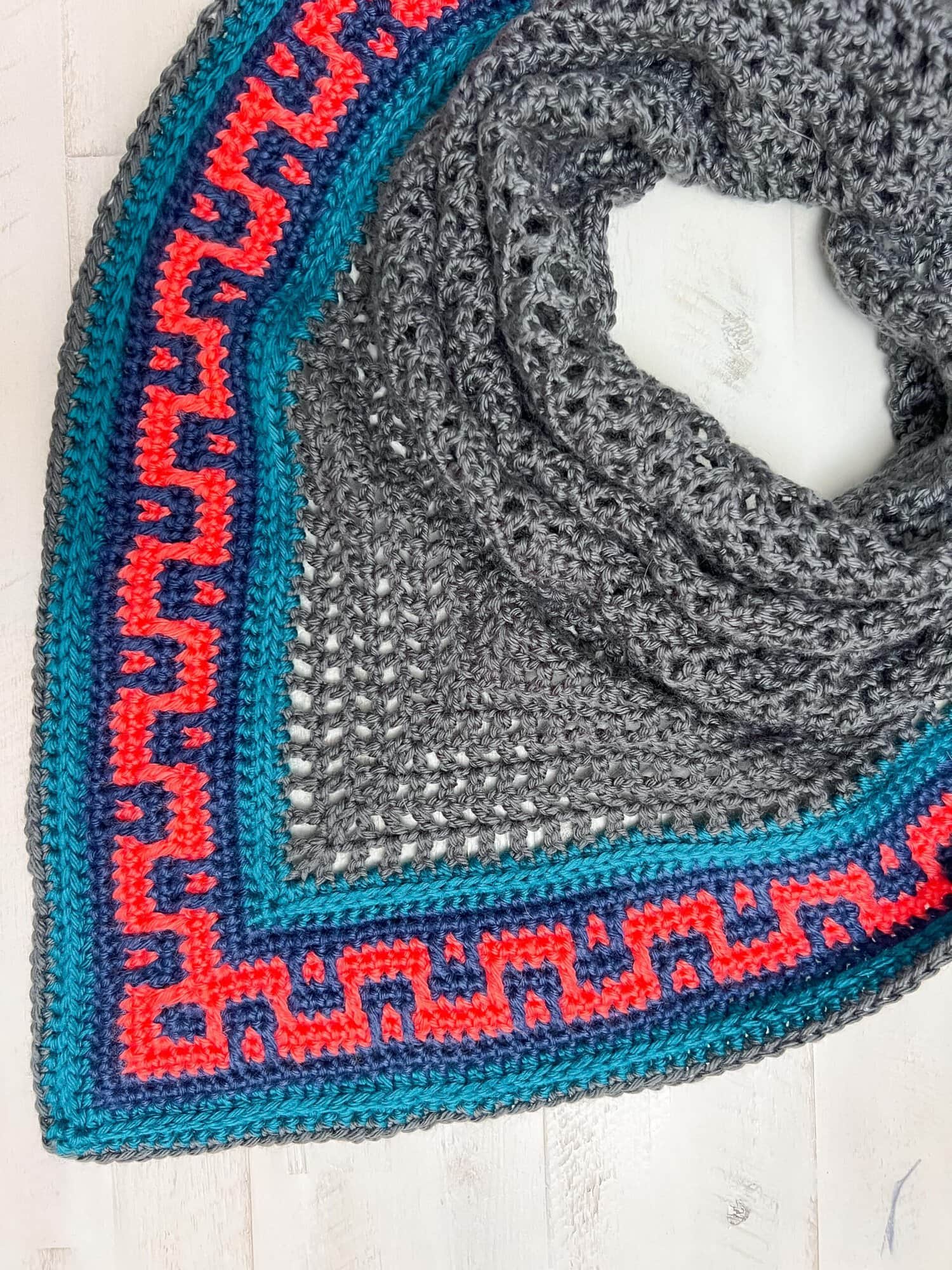 Coral Ridge free crochet triangle shawl pattern detail — flat-lay showing the heathered gray body and blue and red Greek-key geometric colorblock border