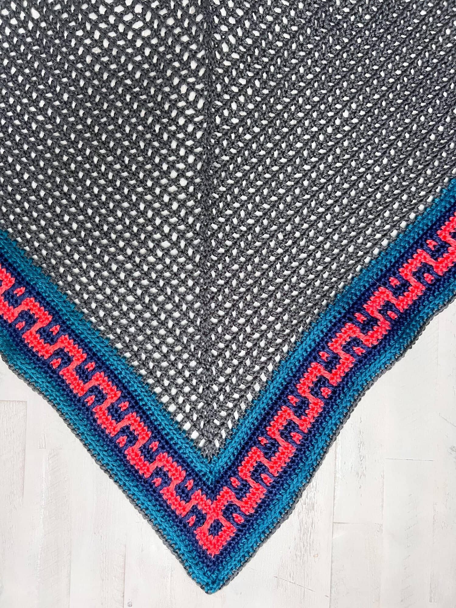 Coral Ridge free crochet triangle shawl pattern detail — gray mesh body with the start of the blue and pink Greek-key colorblock border