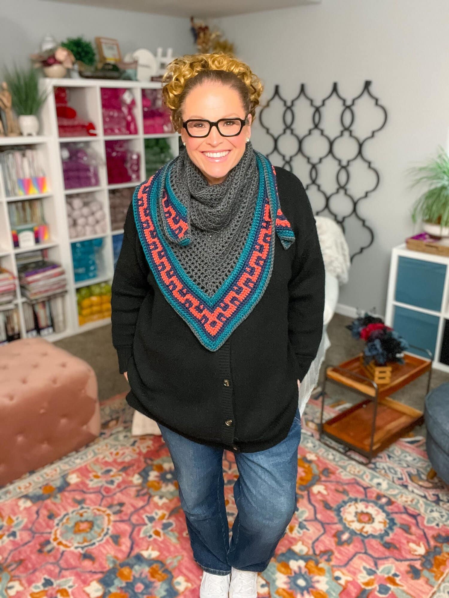 Coral Ridge crochet shawl free pattern modeled in a yarn-filled craft room — gray triangle shawl with teal and red textured border by Marly Bird
