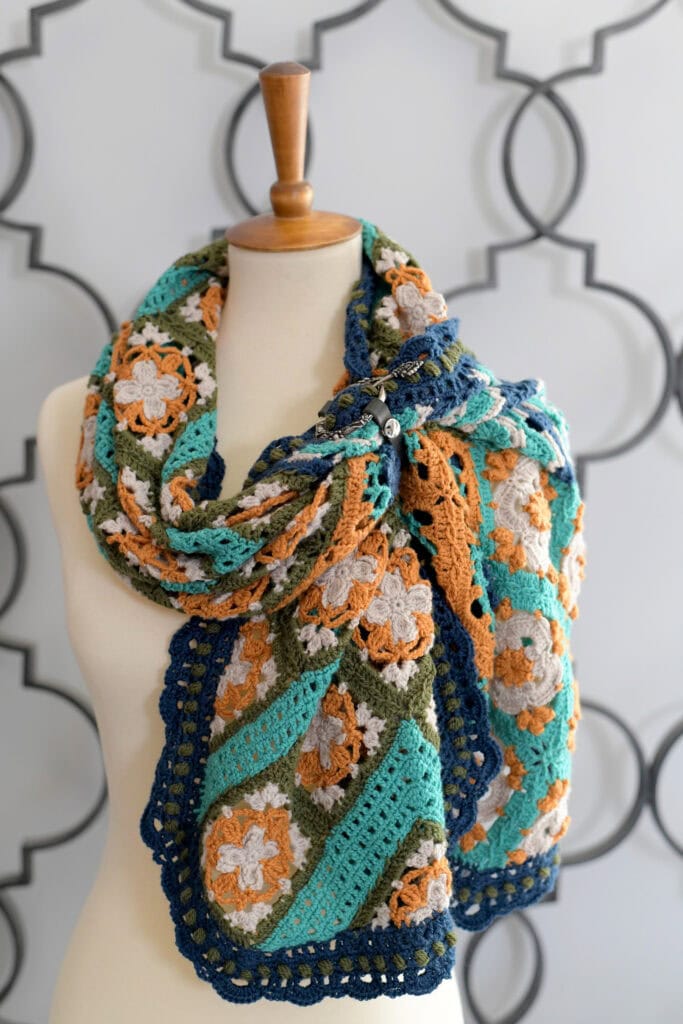 Tunisian crochet scarf with floral and geometric patterns in orange, green, blue, teal, and white on mannequin.