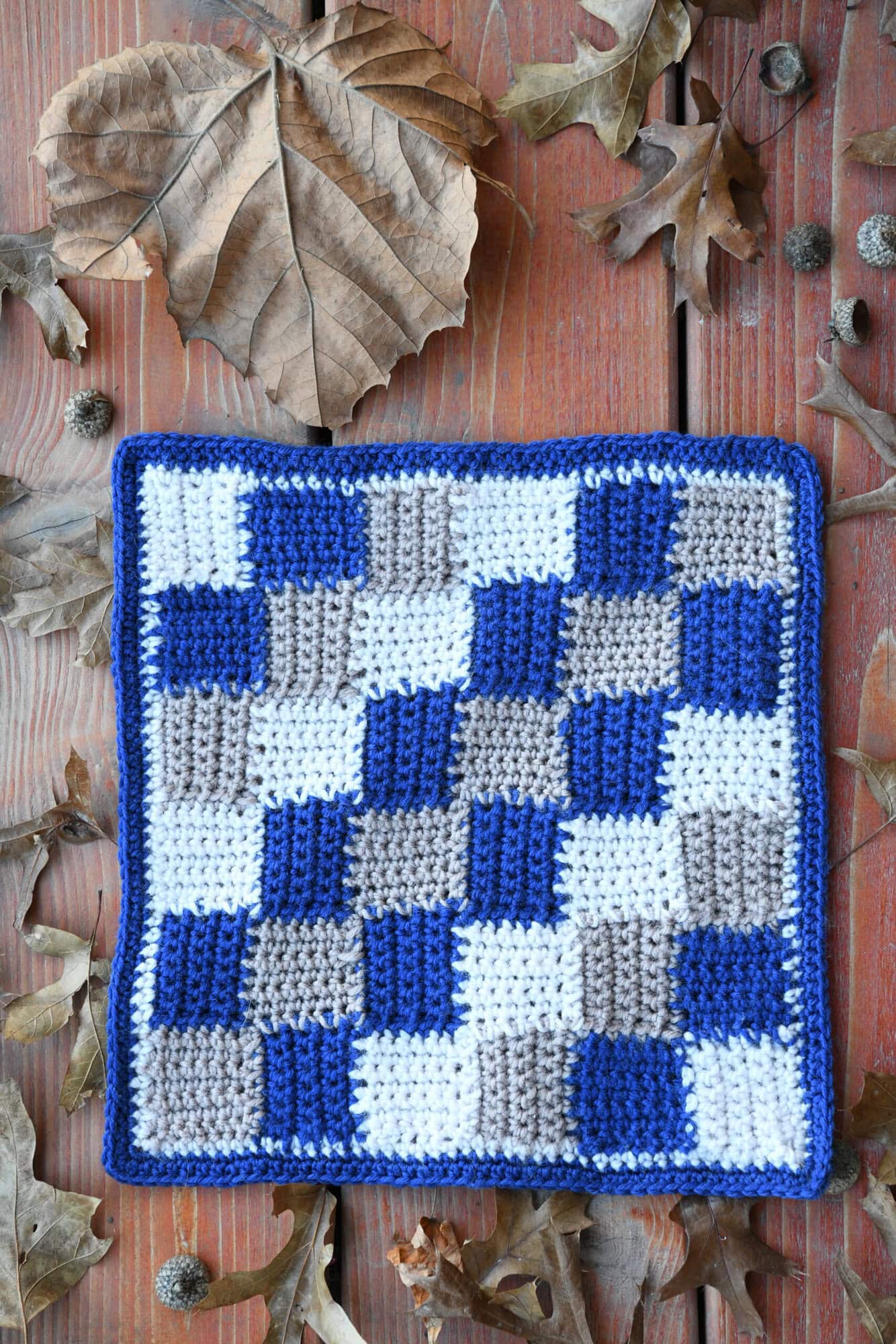 Single Crochet Entrelac square in blue, white, and gray yarn displayed on wood with textured checkerboard pattern.
