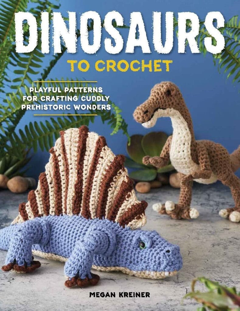 Cover of "Dinosaurs to Crochet" by Megan Kreiner features two crocheted dinosaurs: a blue Stegosaurus in the foreground and Rori the Raptor in the background, with leafy plants and rocks around them. Text reads, "Playful patterns for crafting cuddly prehistoric wonders. -Marly Bird