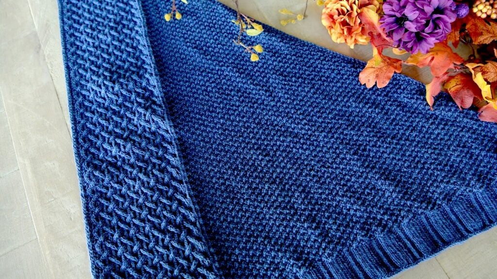 Eowyn cable knit shawl displayed flat in navy blue, showing the snug cable and double moss stitch texture in detail.