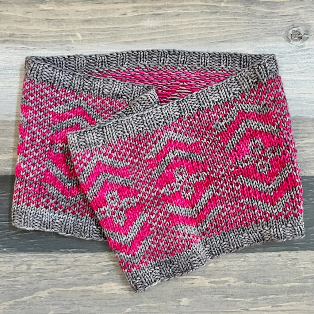 Geometric cowl with stranded knitting in gray and bright pink, featuring diamond motifs and dotted centers on soft textured fabric.