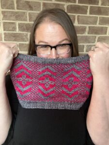 Tunisian crochet cowl in pink and gray geometric pattern, worn as a neck warmer; stitch detail and texture visible.