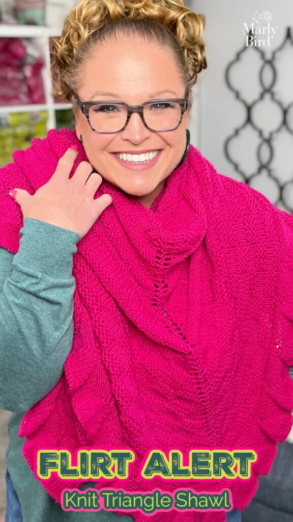 Bright pink worsted knit triangle shawl draped on a model; features smooth texture and subtle stitch definition.
