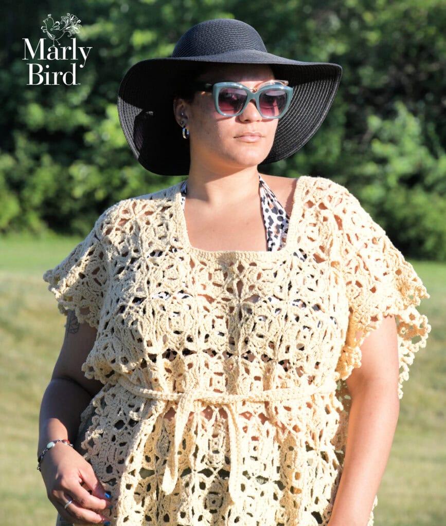 A woman models a yellow lacy crochet cover-up, showing its openwork stitch pattern and airy texture in sunlight.
